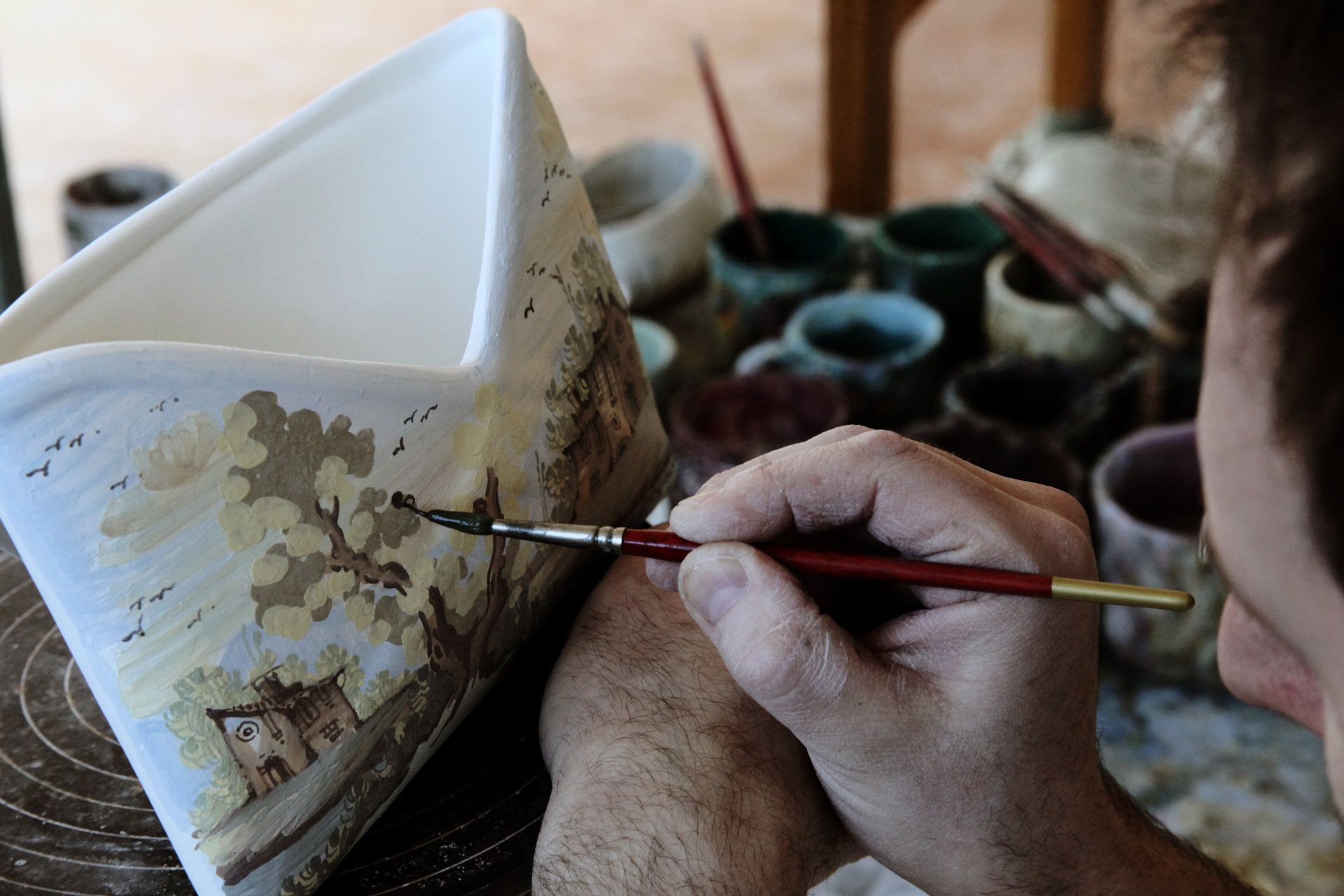 pittore che dipinge una paesaggio su un un porta tovaglioli di maiolica di argilla a Castelli in Abruzzo De Fabritiis